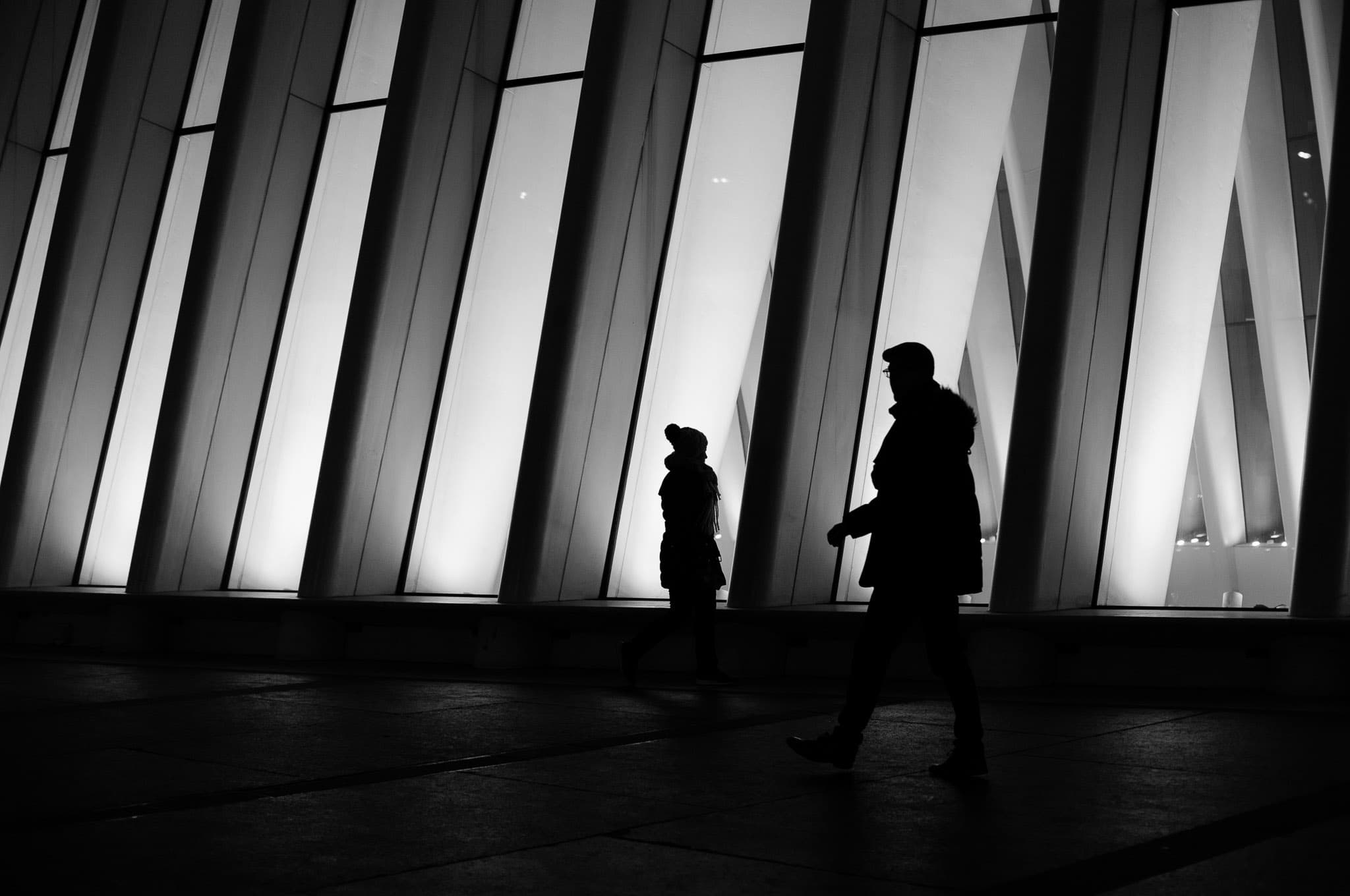 Two people face the side of Westfield Oculus, crossing in opposite paths.