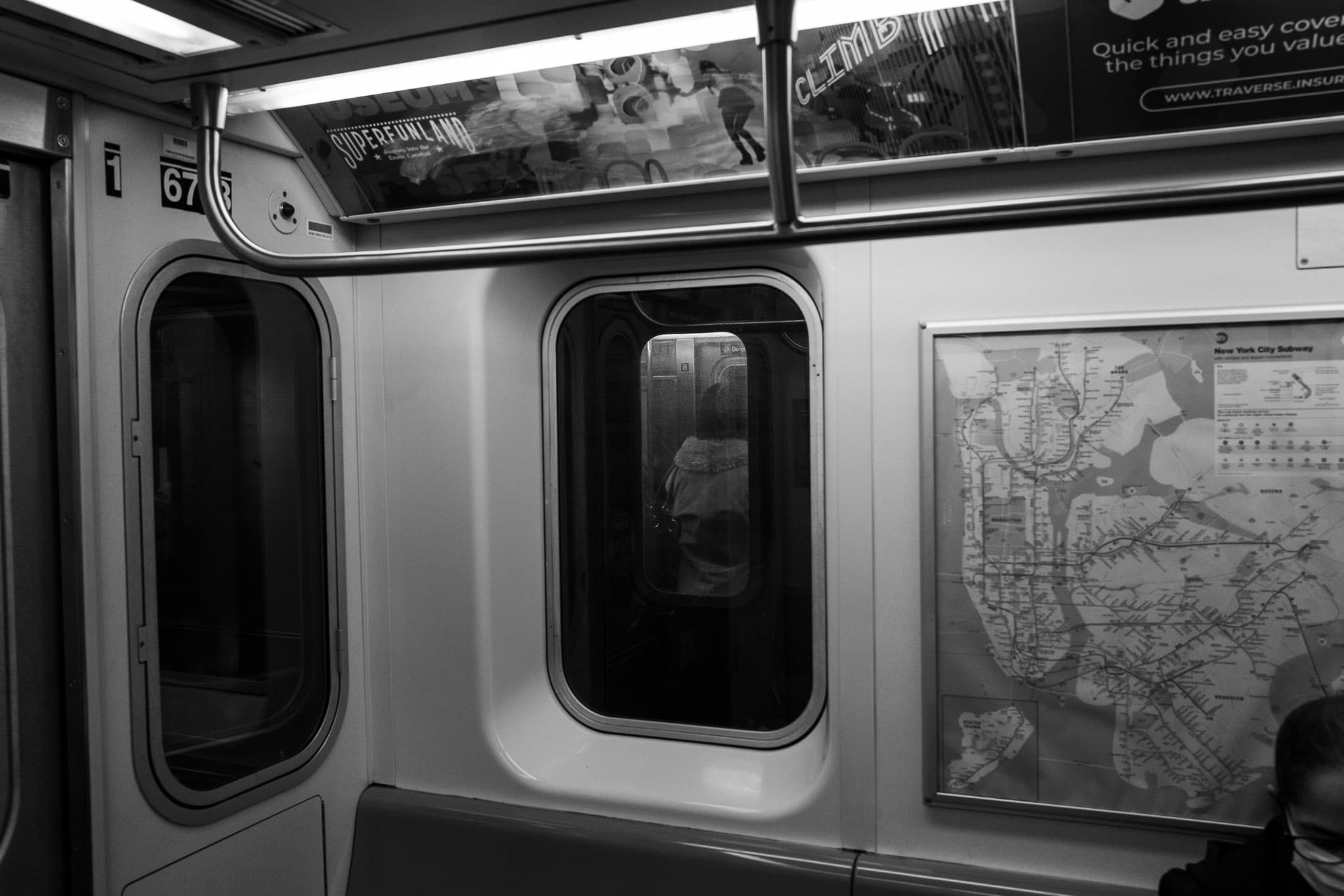 View of a New York City Transit subway car window where the interior of another subway car can be seen with a person leaning by the side doors.