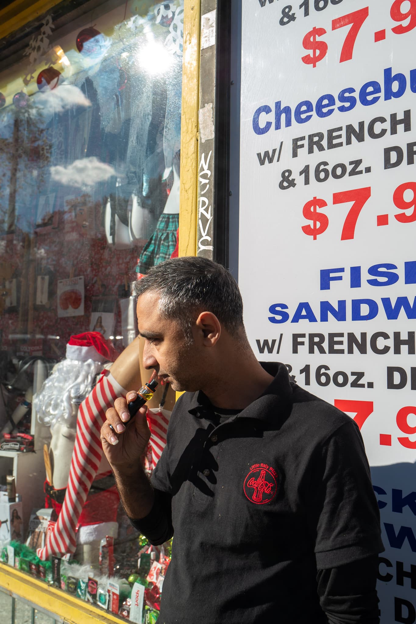 A person vapes in front the intersection between an adult toy store and fast food spot.