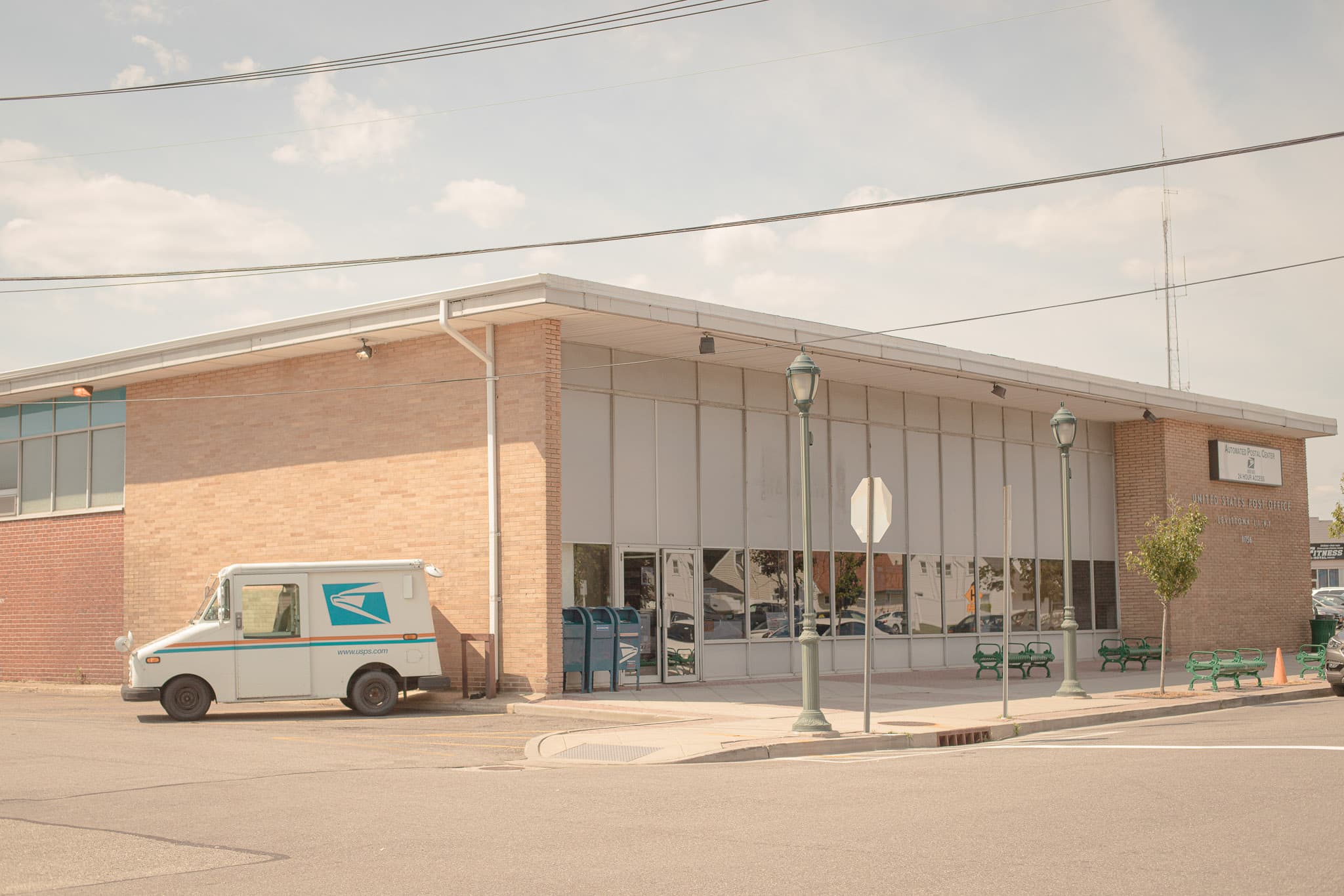 A picture of a United States Postal Service post office with a USPS vehicle on the side of the building.